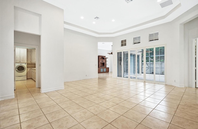 spare room with a high ceiling, washer / clothes dryer, a raised ceiling, and light tile flooring