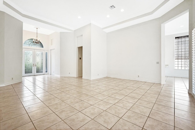 tiled empty room with a raised ceiling, french doors, and a chandelier