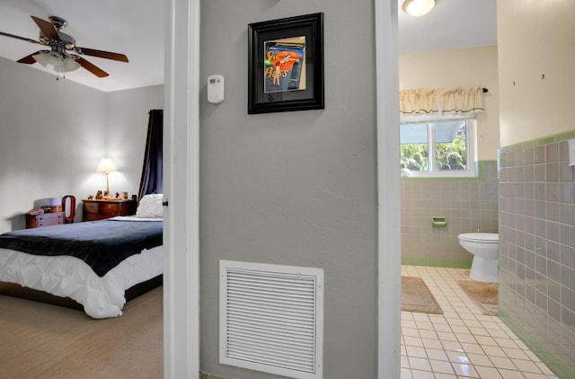 bedroom featuring light tile flooring, ceiling fan, ensuite bathroom, and tile walls