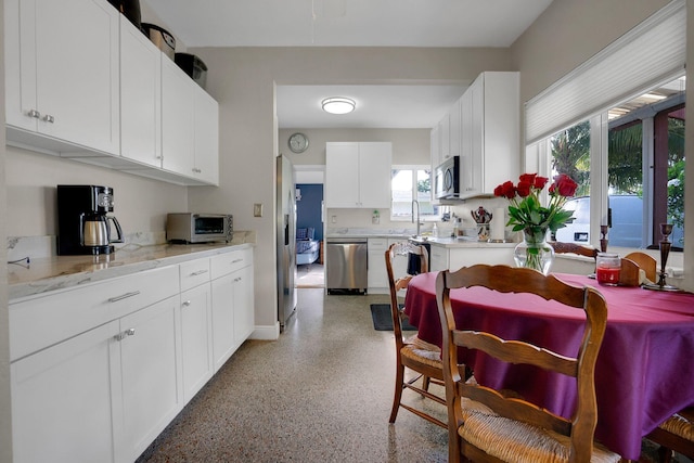 kitchen with white cabinets, light stone countertops, stainless steel appliances, and sink