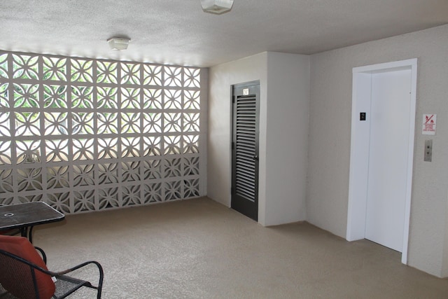 empty room with light carpet, a textured ceiling, and elevator