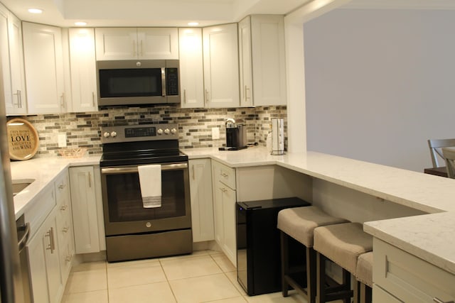 kitchen with backsplash, light tile floors, appliances with stainless steel finishes, and light stone countertops