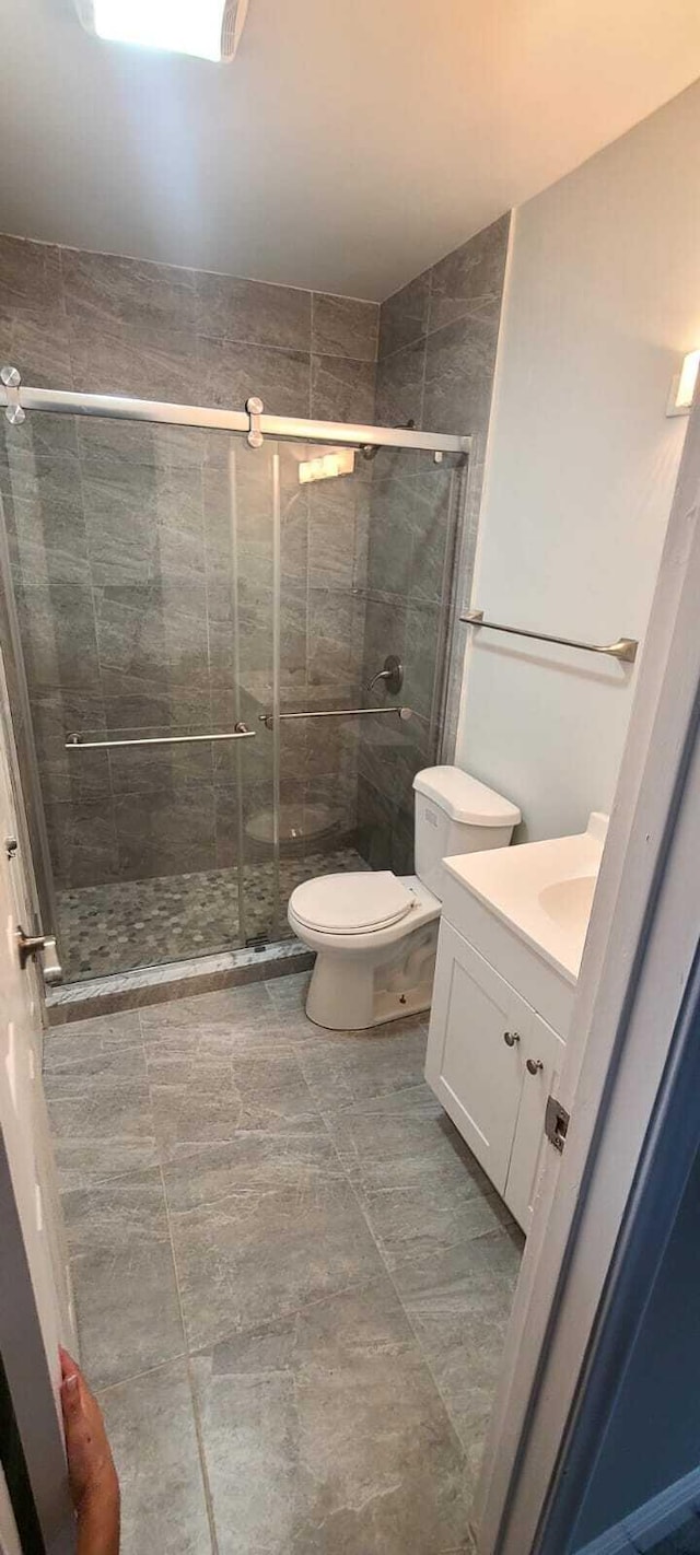 bathroom featuring toilet, tile floors, a shower with shower door, and vanity