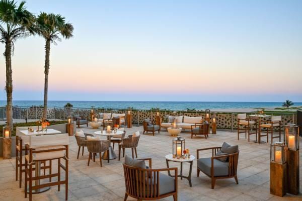 patio terrace at dusk with outdoor lounge area, a water view, and a beach view