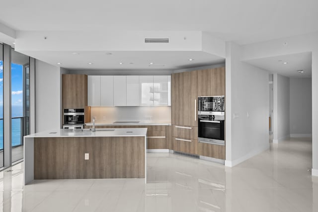 kitchen featuring white cabinets, a water view, a kitchen island with sink, and a healthy amount of sunlight