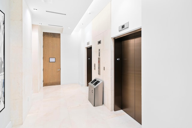 hallway featuring light tile patterned flooring, a towering ceiling, and elevator