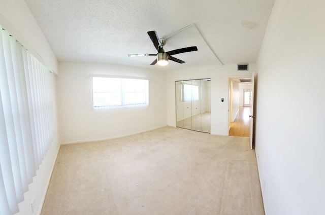 unfurnished bedroom with light colored carpet, a closet, ceiling fan, and a textured ceiling