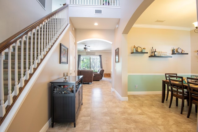 tiled foyer with ceiling fan, a towering ceiling, and ornamental molding