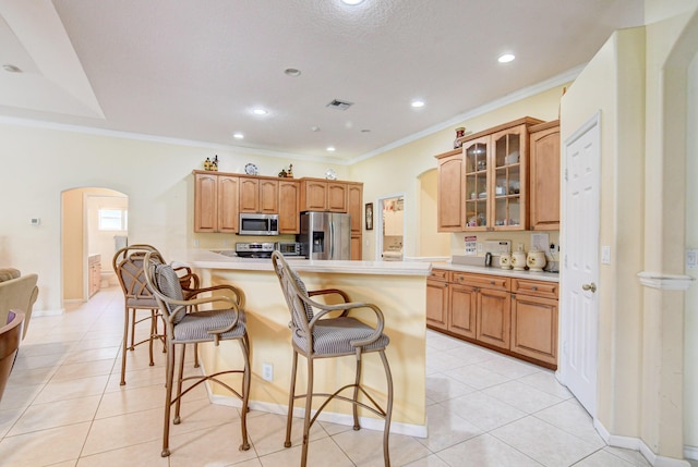 kitchen featuring kitchen peninsula, crown molding, stainless steel appliances, light tile flooring, and a kitchen bar