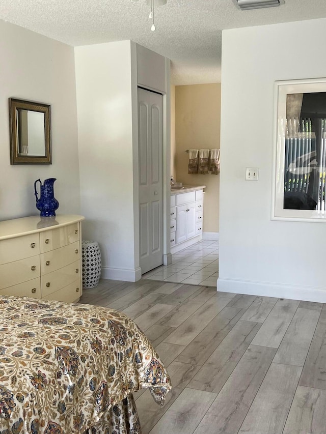 bedroom with connected bathroom, a closet, light hardwood / wood-style flooring, and a textured ceiling