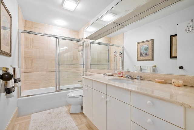 full bathroom with vanity, bath / shower combo with glass door, and toilet