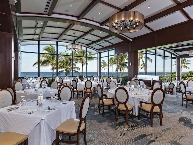 interior space with coffered ceiling, vaulted ceiling with beams, a notable chandelier, dark carpet, and a water view