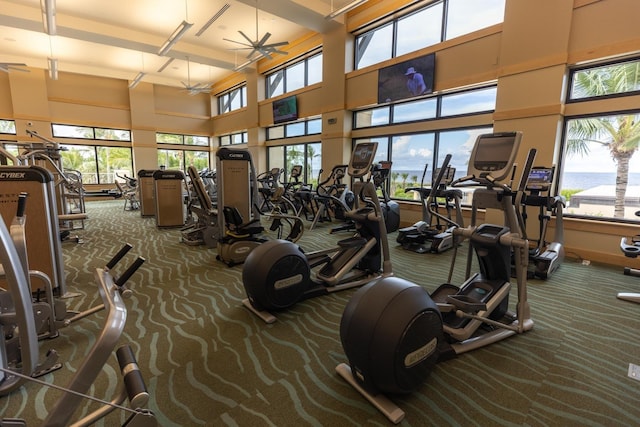 gym with a water view, ceiling fan, dark carpet, and a high ceiling