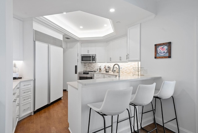 kitchen with kitchen peninsula, dark hardwood / wood-style floors, a kitchen breakfast bar, appliances with stainless steel finishes, and tasteful backsplash