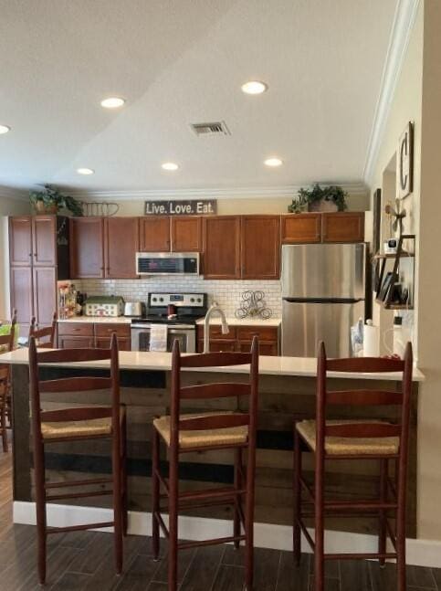 kitchen with crown molding, tasteful backsplash, appliances with stainless steel finishes, and a breakfast bar