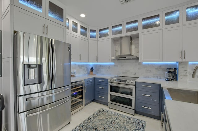 kitchen featuring white cabinets, appliances with stainless steel finishes, backsplash, light tile flooring, and wall chimney range hood