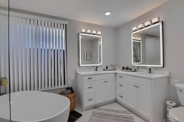 bathroom featuring a bath to relax in, dual sinks, vanity with extensive cabinet space, and toilet