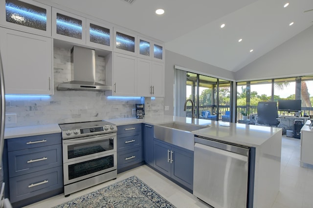 kitchen featuring backsplash, light tile flooring, stainless steel appliances, white cabinets, and wall chimney range hood