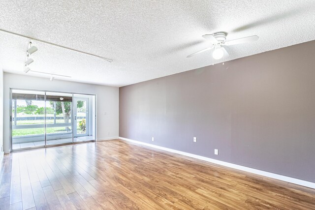 empty room featuring a textured ceiling, rail lighting, ceiling fan, and light wood-type flooring