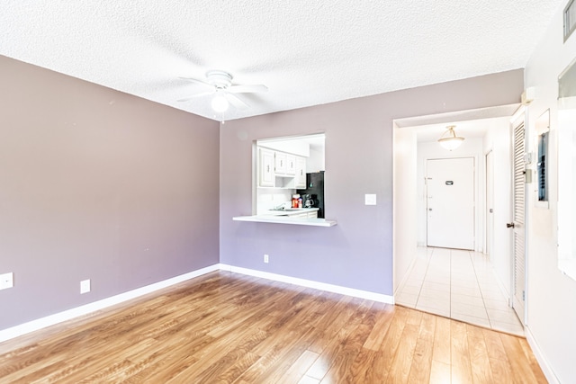 empty room with a textured ceiling, ceiling fan, and light hardwood / wood-style flooring