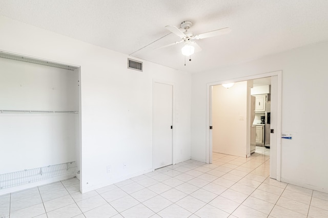 unfurnished bedroom with light tile flooring, a closet, and ceiling fan