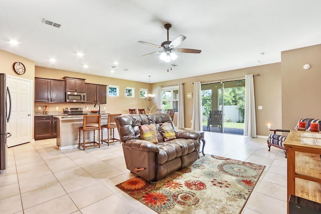 living room featuring light tile flooring, ceiling fan with notable chandelier, and sink