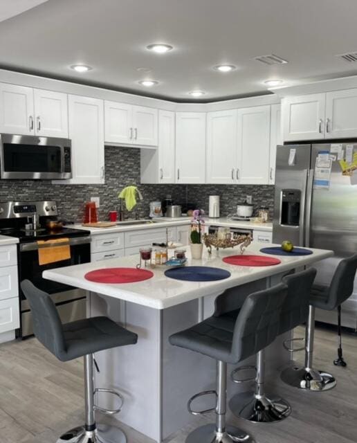 kitchen with a kitchen island, stainless steel appliances, a kitchen breakfast bar, and white cabinetry