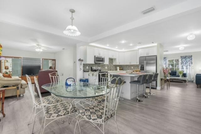 dining space featuring beam ceiling, ceiling fan with notable chandelier, and light hardwood / wood-style flooring