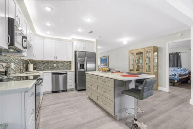 kitchen featuring stainless steel appliances, a breakfast bar, light hardwood / wood-style flooring, white cabinets, and backsplash