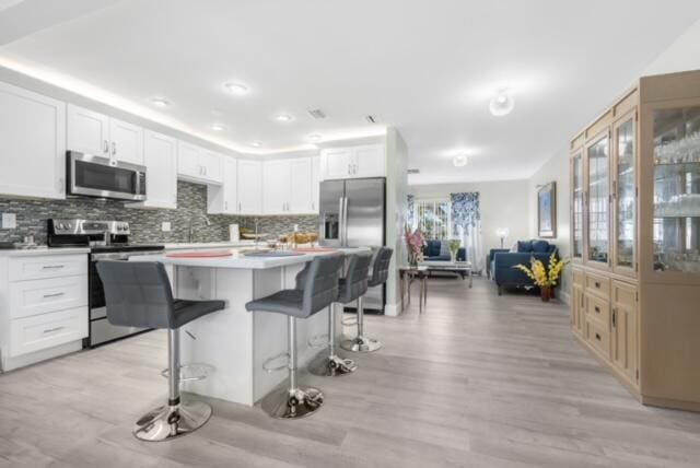 kitchen with a kitchen breakfast bar, white cabinets, appliances with stainless steel finishes, light hardwood / wood-style flooring, and a center island