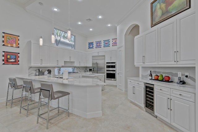 kitchen with white cabinets, appliances with stainless steel finishes, wine cooler, light stone countertops, and ornamental molding