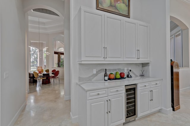 bar featuring a notable chandelier, light tile floors, beverage cooler, white cabinetry, and ornamental molding