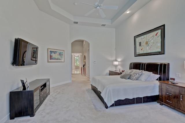 carpeted bedroom with a high ceiling, ceiling fan, a tray ceiling, and ensuite bathroom