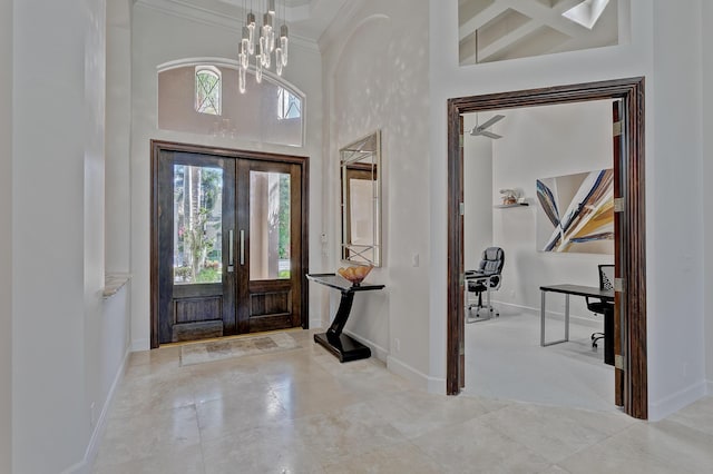 tiled foyer entrance with a towering ceiling, a notable chandelier, coffered ceiling, and french doors