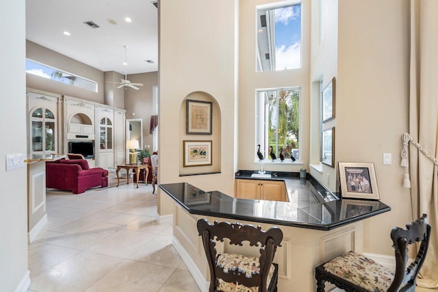 interior space featuring kitchen peninsula, ceiling fan, light tile floors, and a high ceiling