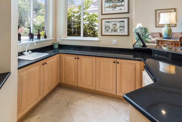 kitchen with sink, light tile floors, dark stone counters, black dishwasher, and light brown cabinets