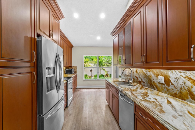 kitchen with sink, light stone counters, backsplash, light hardwood / wood-style floors, and stainless steel appliances