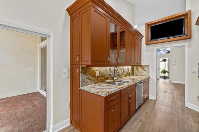 kitchen with stainless steel dishwasher, light stone countertops, tasteful backsplash, light wood-type flooring, and sink