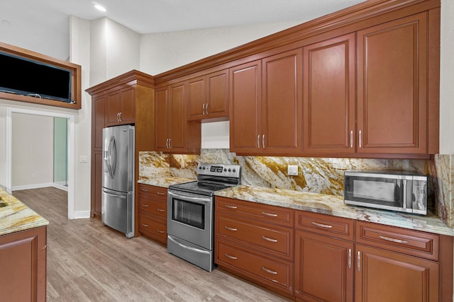 kitchen with backsplash, light wood-type flooring, light stone counters, and stainless steel appliances