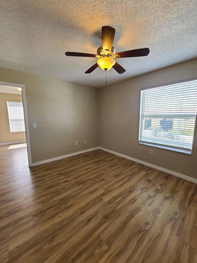 spare room with a textured ceiling, dark hardwood / wood-style floors, ceiling fan, and a healthy amount of sunlight