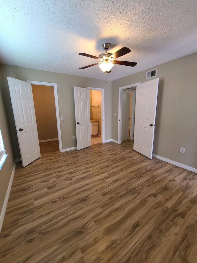 unfurnished bedroom with a spacious closet, ceiling fan, dark wood-type flooring, and a textured ceiling