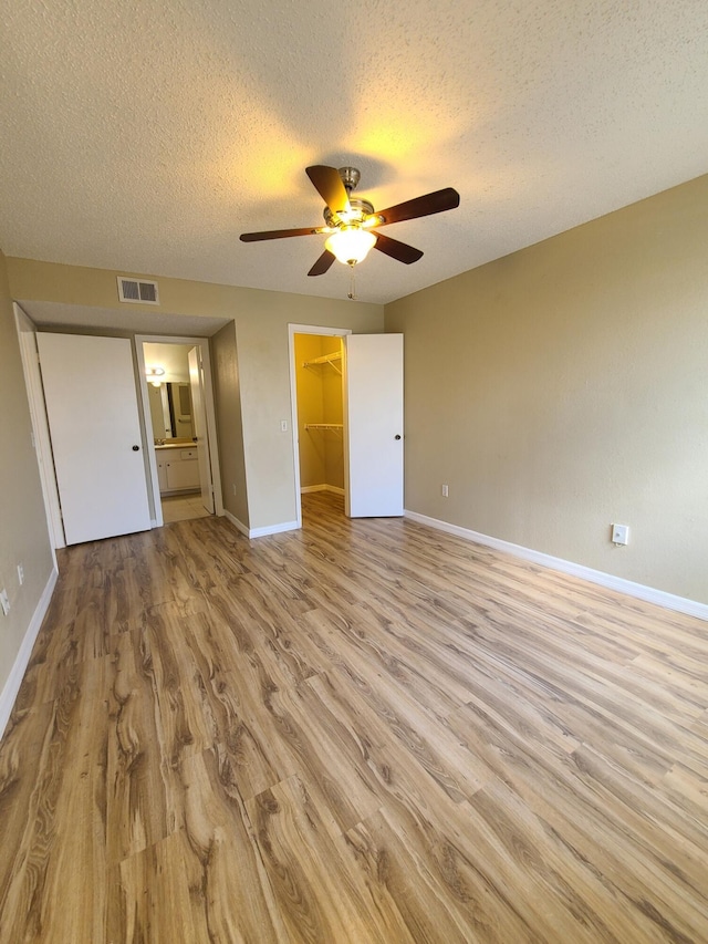 unfurnished bedroom with a closet, a walk in closet, ceiling fan, light hardwood / wood-style floors, and ensuite bathroom