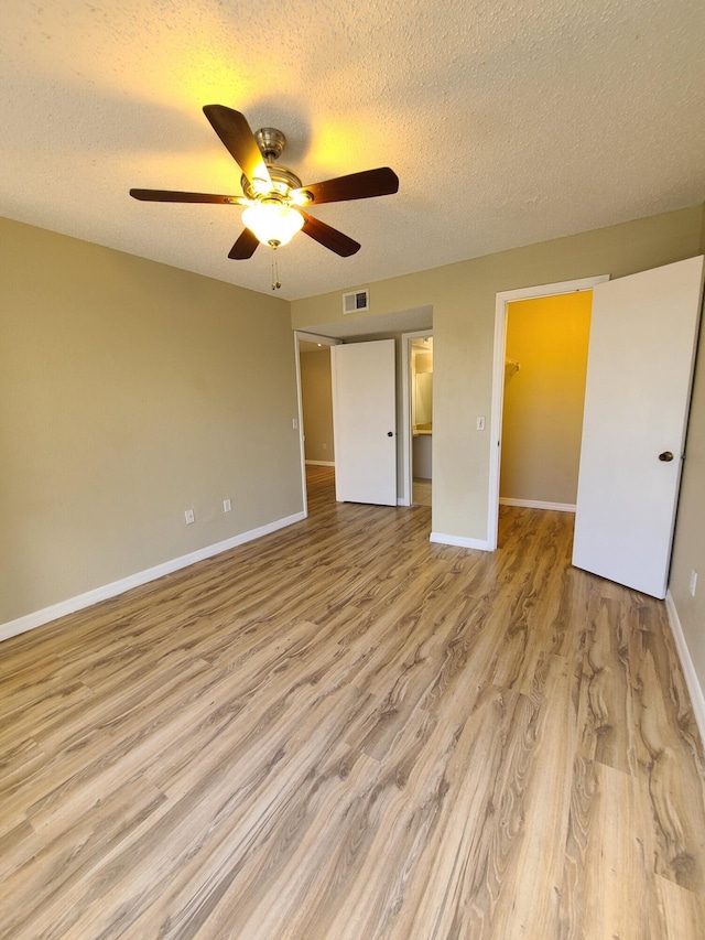 unfurnished bedroom featuring ceiling fan, a walk in closet, light hardwood / wood-style floors, a textured ceiling, and a closet