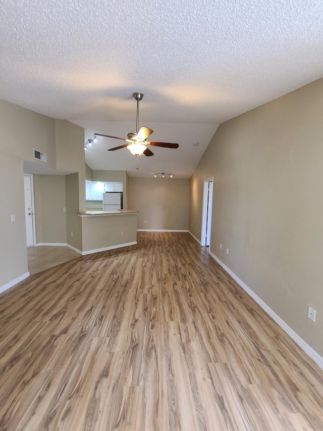 interior space featuring lofted ceiling, ceiling fan, light hardwood / wood-style flooring, and a textured ceiling