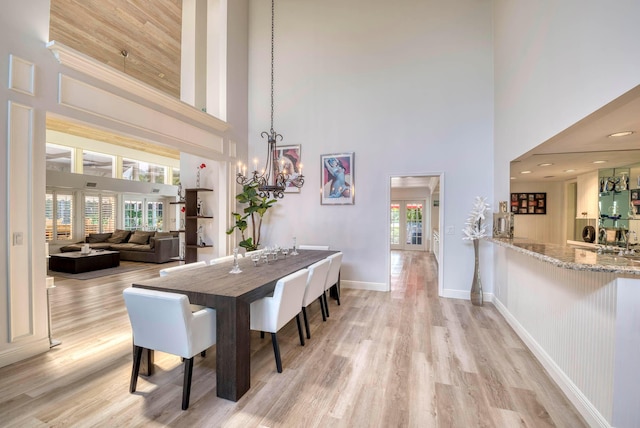 dining area featuring light wood-type flooring, a towering ceiling, and an inviting chandelier