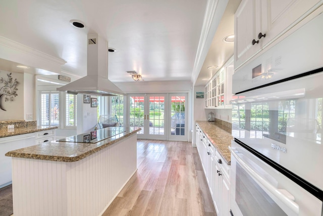 kitchen with black electric cooktop, island range hood, white cabinets, and a kitchen island