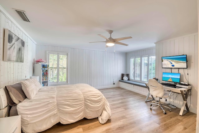 bedroom featuring light wood-type flooring, ceiling fan, ornamental molding, and wood walls