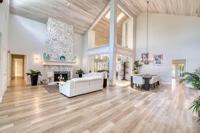 living room with an inviting chandelier, high vaulted ceiling, a stone fireplace, and light hardwood / wood-style floors