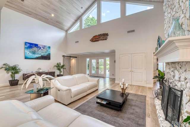 living room with a barn door, a stone fireplace, wood ceiling, and plenty of natural light