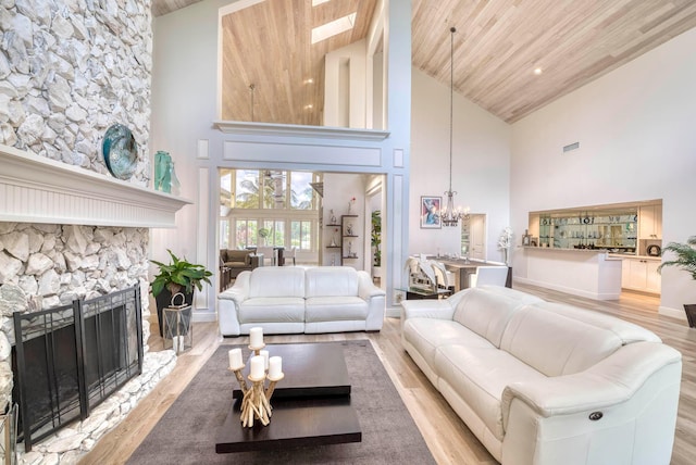 living room featuring a stone fireplace, wood ceiling, high vaulted ceiling, and light hardwood / wood-style flooring